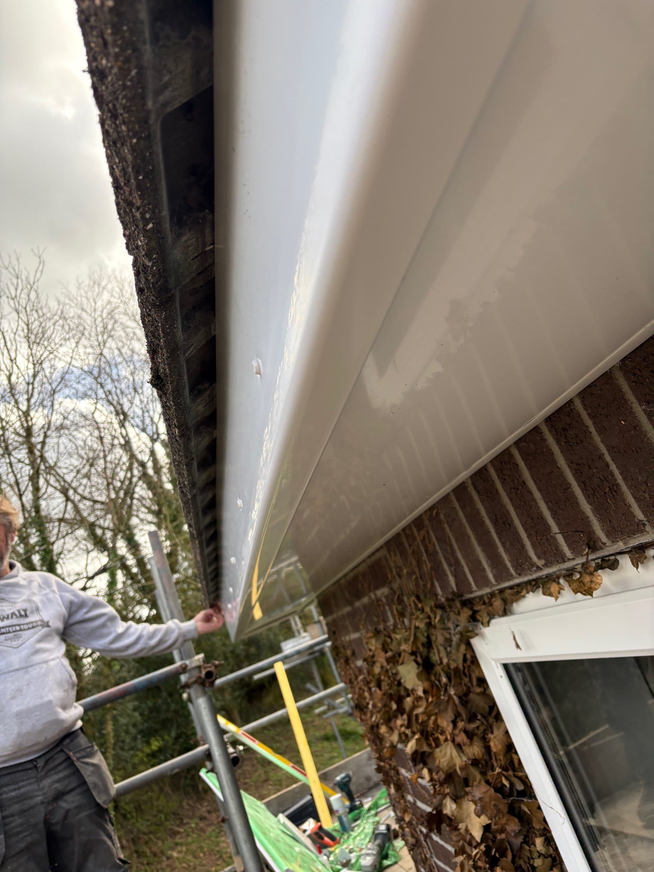 Close-up new UPVC fascia and soffit installed by Mets Roofing — workman finishing the run.