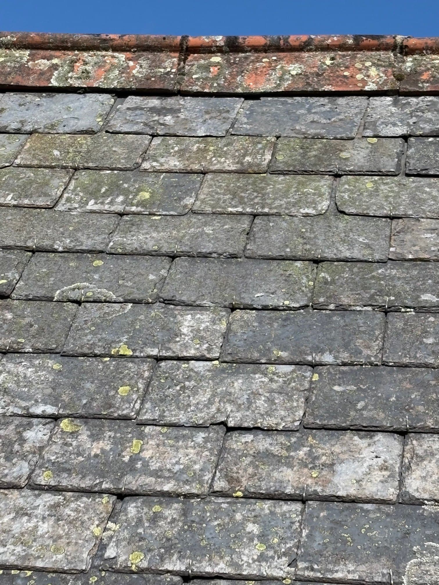 Close-up old weathered slates being replaced beside red brick chimney — slate repair in progress.